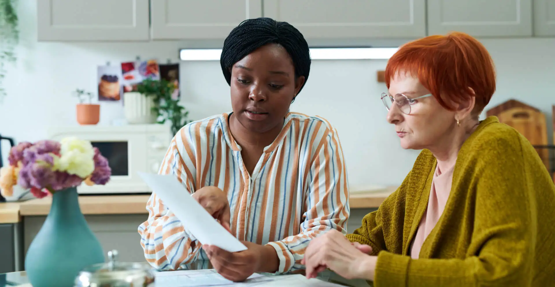 african young volunteer sitting at kitchen table together with senior woman and helping with bills